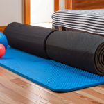 **Prompt:** Foldable foam roller collapsed and stored under a bed next to other home workout equipment (yoga mat, massage ball). Emphasize space-saving and organization in a small apartment setting.
